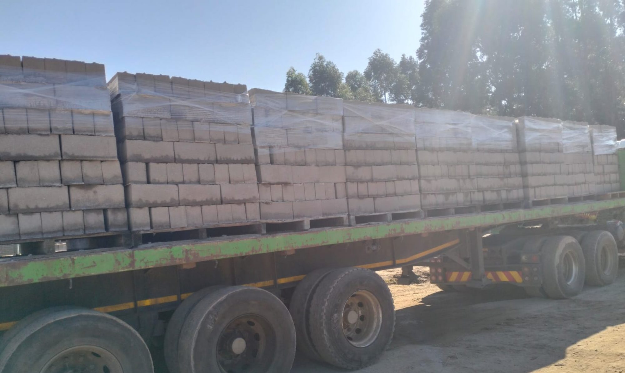 A green flat bed truck with pallets of building blocks packed neatly on it